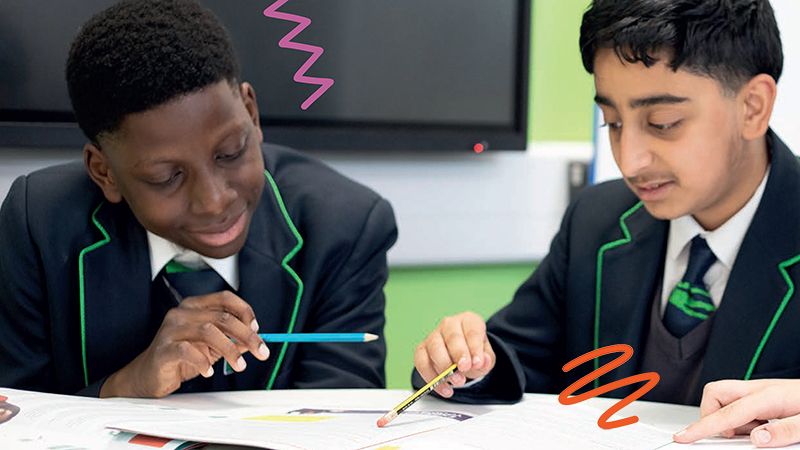 Two boys wearing school uniforms, sitting at a desk