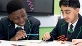 Two boys wearing school uniforms, sitting at a desk