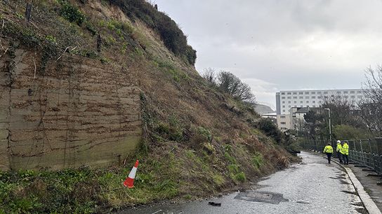 A photo of a road with a huge landslip which is encroaching the road.