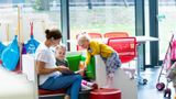 An adult shares a book with two children in a library reading area, encouraging reading and storytelling together.