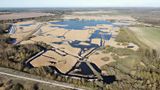 Aerial view of a large wetland nature reserve showing interconnected lakes, reedbeds and waterways surrounded by farmland and woodland. The landscape features winding channels of water weaving through golden reed beds, with open countryside stretching to the horizon under a clear sky.