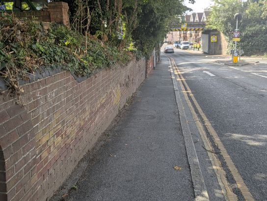 An image of a pavement and road with a bridge in the distance.