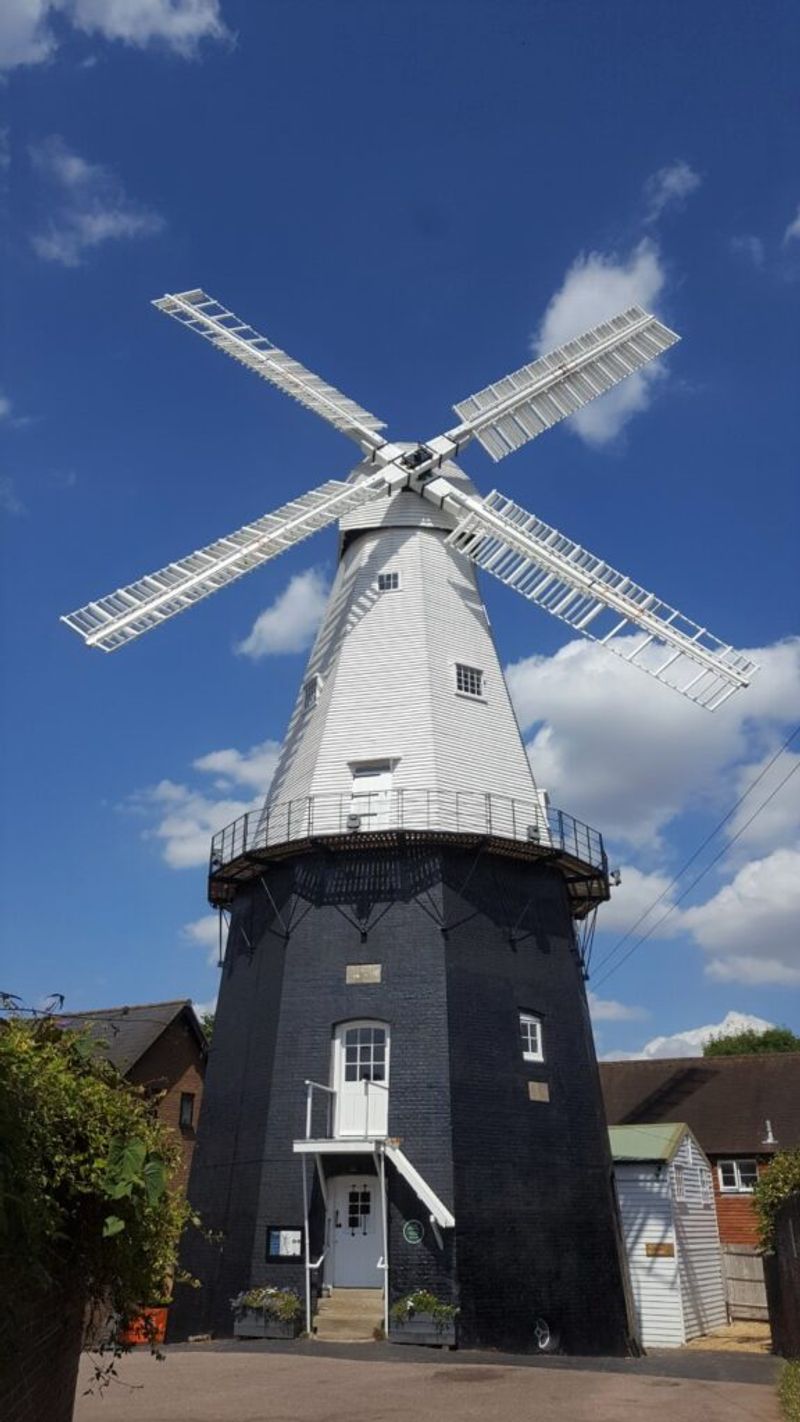 Image of Cranbrook windmill. A black base windmill, with white blades surrounded by a bright blue sky