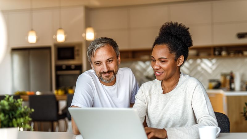 Man and woman sit infront of a laptop in their home