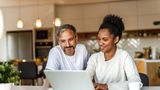 Man and woman sit infront of a laptop in their home