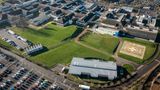 A drone image of a hospital building. There is a big H on the ground. Lots of houses are in the top of the photo.