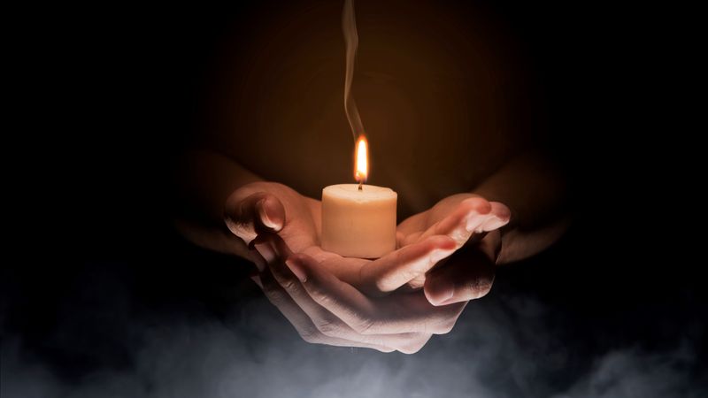 A lit candle sits in a hand against a dark background