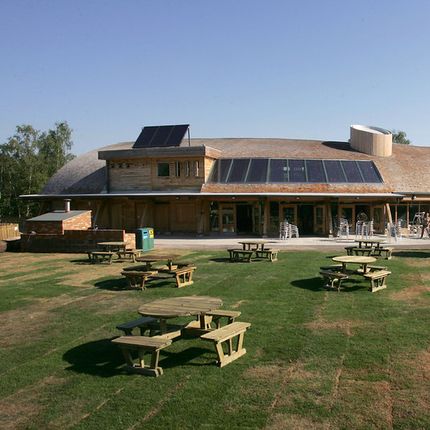 Modern wooden building with solar panels on the roof and picnic tables on a grassy lawn.