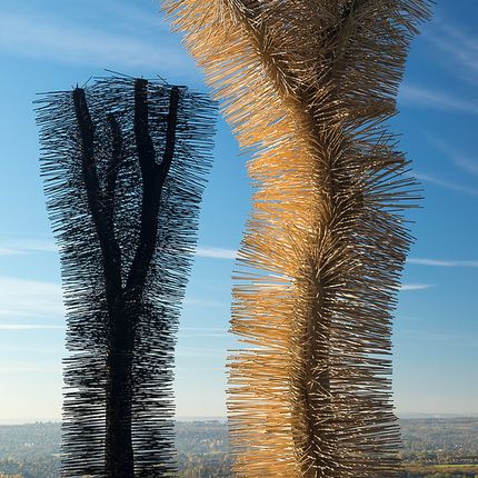 Two tall abstract sculptures covered in protruding wooden sticks, set against a clear blue sky.