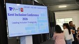 A screen says Kent Inclusion Conference as people walk by