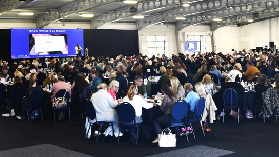 Hundreds of people sit in a conference hall watching a presentation