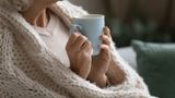 Older person holding a hot cup of tea and wrapped in a blanket