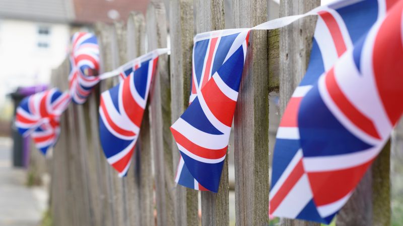 Union Jack square bunting flags hung over a wooden fence and blowing in the breeze
