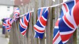 Union Jack square bunting flags hung over a wooden fence and blowing in the breeze