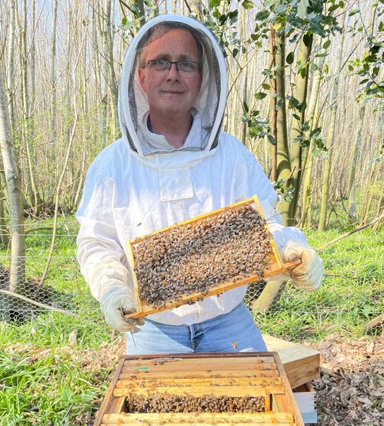 Neil Sampson from Solar Gates UK in protective beekeeping gear with a hive and some of his bees on a frame