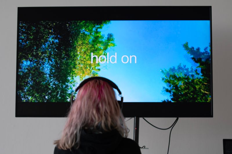 A person wearing headphones in front of TV screen that says 'Hold on'
