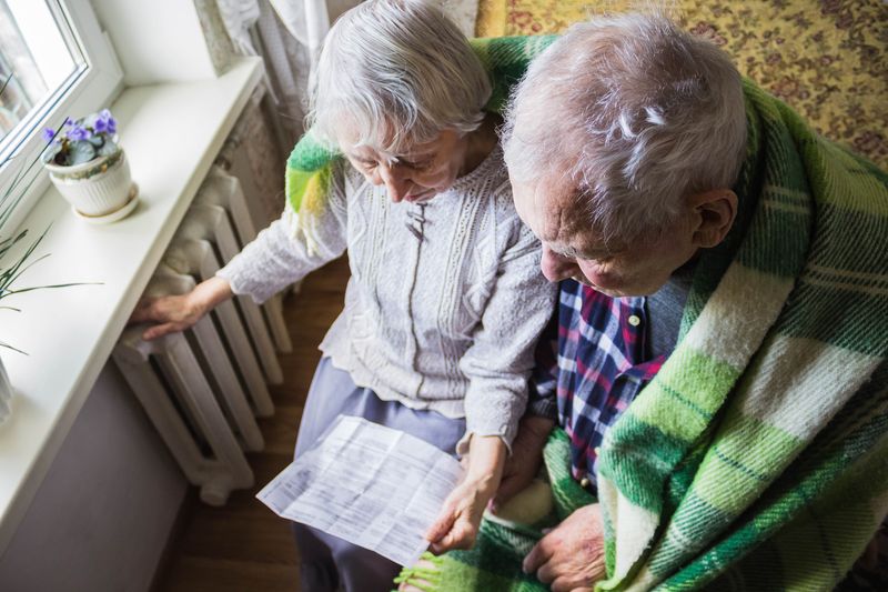 Elderly couple sat in front of radiator looking at heating bill