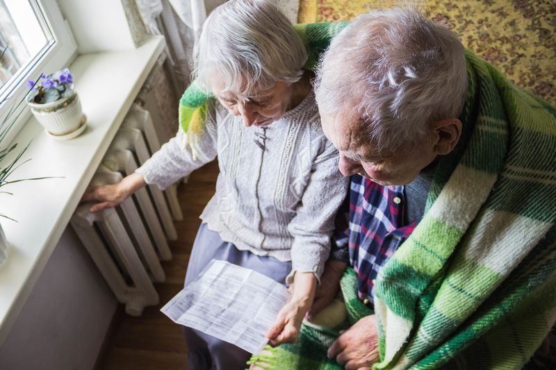 Elderly couple sat in front of radiator looking at heating bill