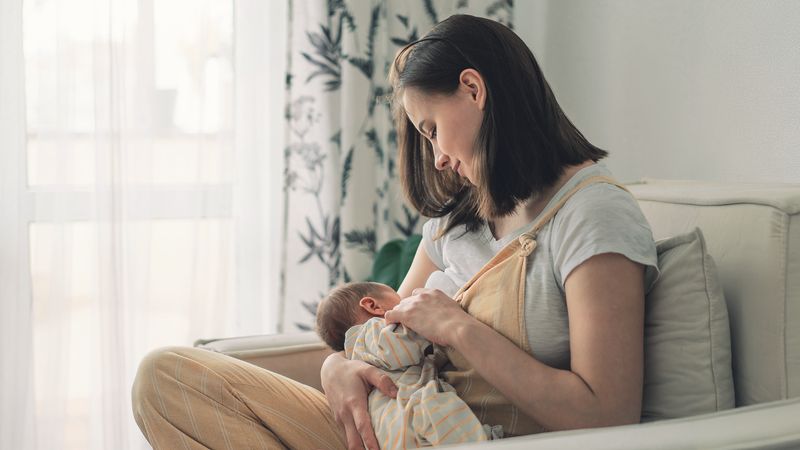 Breastfeeding mum sat on sofa with baby