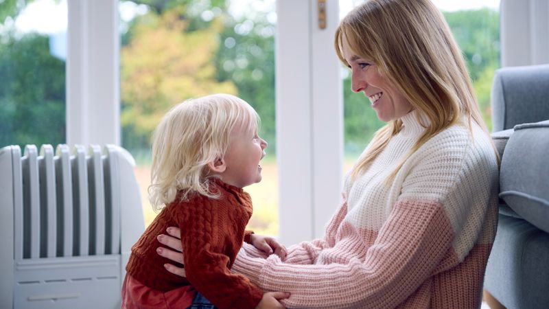 smiling mum and toddler wearing jumpers in front of radiator