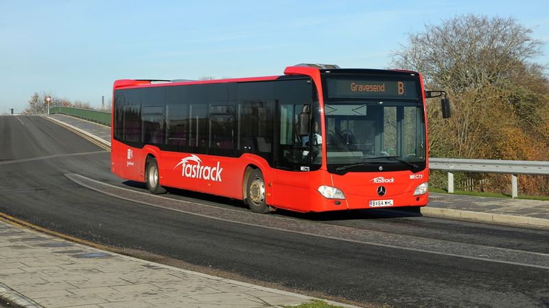 A red bus drives down a road. The bus says 'Gravesend B' on the front at the top.