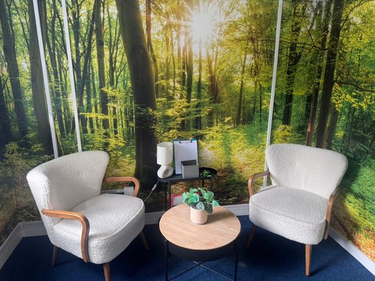 A therapy room with two white chairs and a background of tree wallpaper