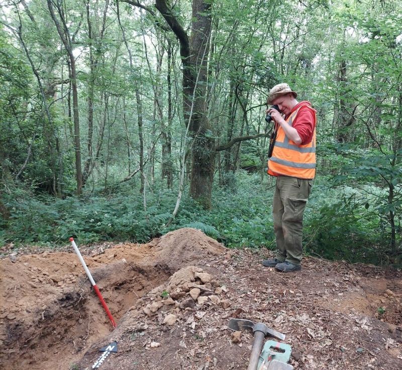 KCC's Community Archaeologist Andrew Mayfield photographs a woodland find in the ground.