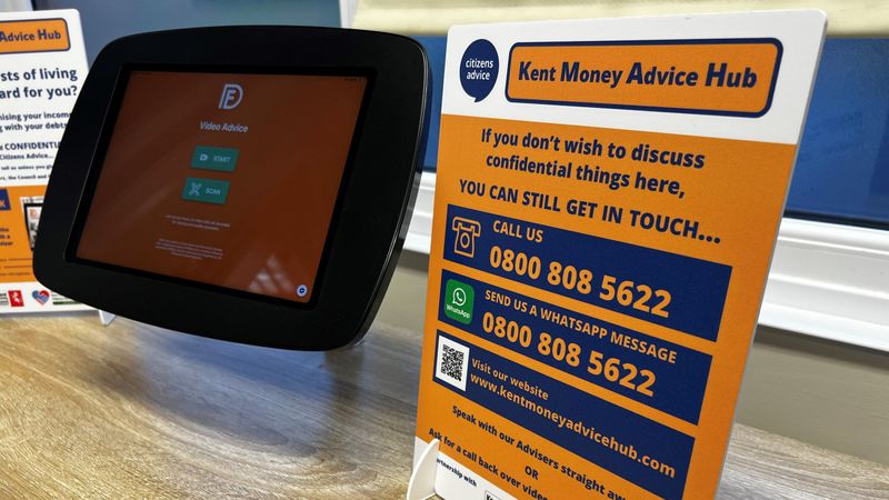 Kent Money Advice Hub poster displayed on countertop with tablet. It says "if you don't wish to discuss confidential things here. You can still get in touch, call 0800 808 5622 whatsapp the same number or visit www.kentmoneyadvicehub.com. Speak with our advisors straight away or ask for a video call back