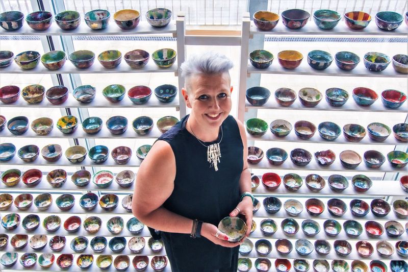 Mona Whitton in front of the 300 colourful bowls that make up the Out of the Fire exhibit