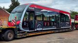 A photograph of a new Fastrack electric bus being delivered on a lorry.