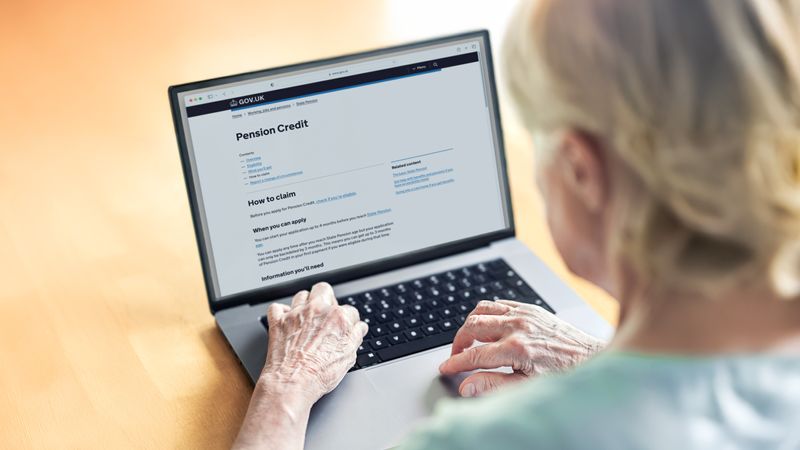 A figure looks at a laptop with the Government's Pensions Credit webpage on the screen.