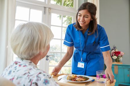 Carer serves dinner to older woman at home 