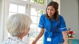 Carer serves dinner to older woman at home 