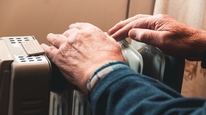 Elderly man warming his hands on a small radiator