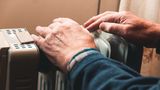 Elderly man warming his hands on a small radiator