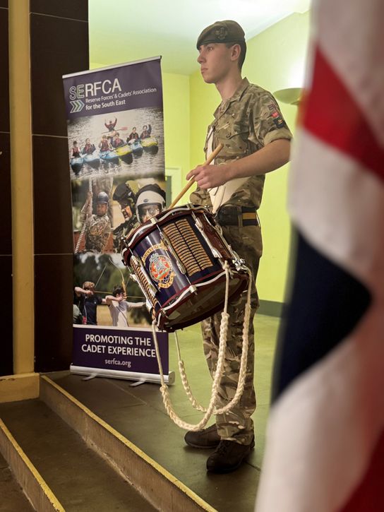 An army cadet drummer stands with his instrument in front of the Union Jack flag before beginning to play