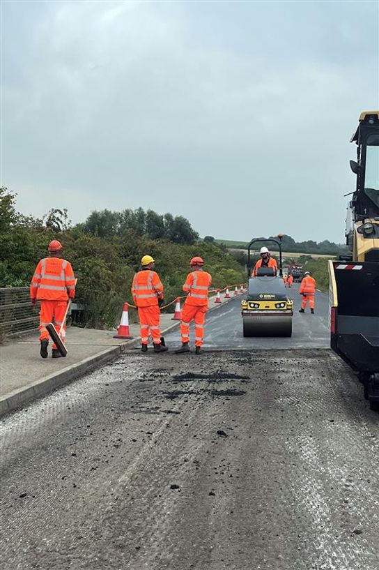 A group of people in orange hi-viz work on resurfacing a road