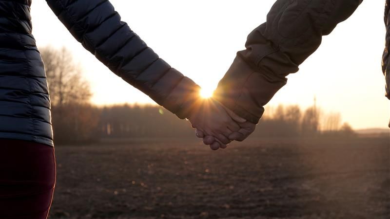 Two people holding hands walking into sunset
