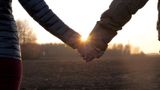Two people holding hands walking into sunset