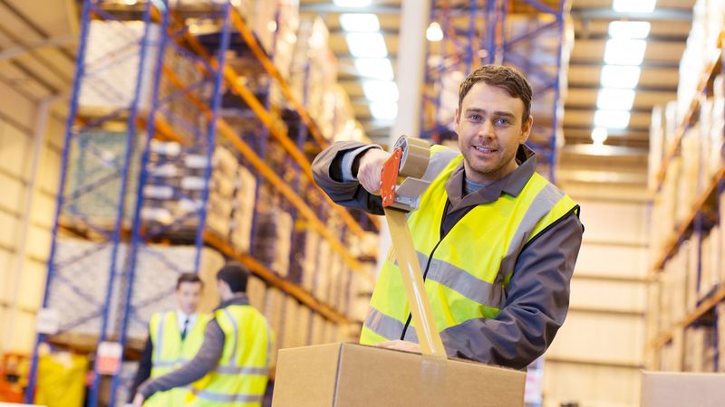 A warehouse worker tapes up a cardboard box