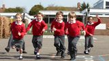 A group of children in red jumpers and black trousers run towards the camera.