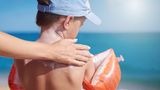 Boy at beach wearing hat has sunscreen applied to his back