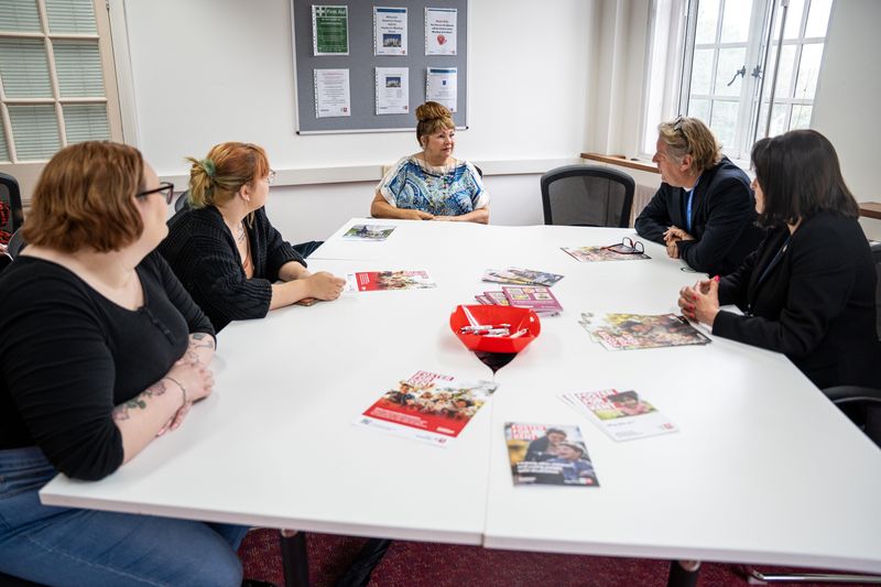 A group of people sat around a square white table talking 