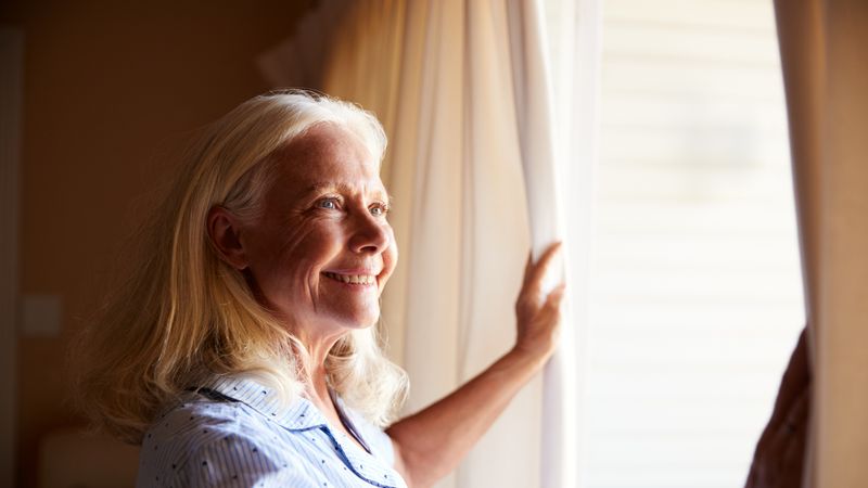 Elderly woman shutting curtains to keep heat out