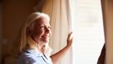 Elderly woman shutting curtains to keep heat out