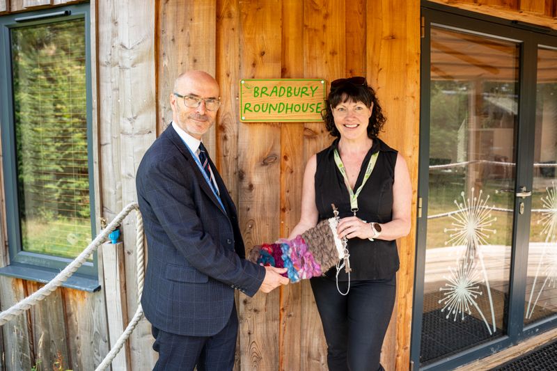 Two people standing in front of a sign that says 'Bradbury Roundhouse' holding a calming tactile object made of dyed wool