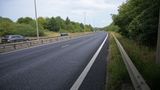 Freshly resurfaced carriageway on the A299 Thanet Way, showing a smooth black road surface, central barrier and street lighting, with trees and vegetation lining both sides of the dual carriageway.