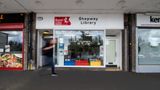 The outside of a Shepway Library - it is a building with a big wide window and the words 'Shepway library' at the top. There is a blurry figure walking past.