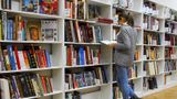 Image of a woman standing infront of shelves of colourful library books, reading a book