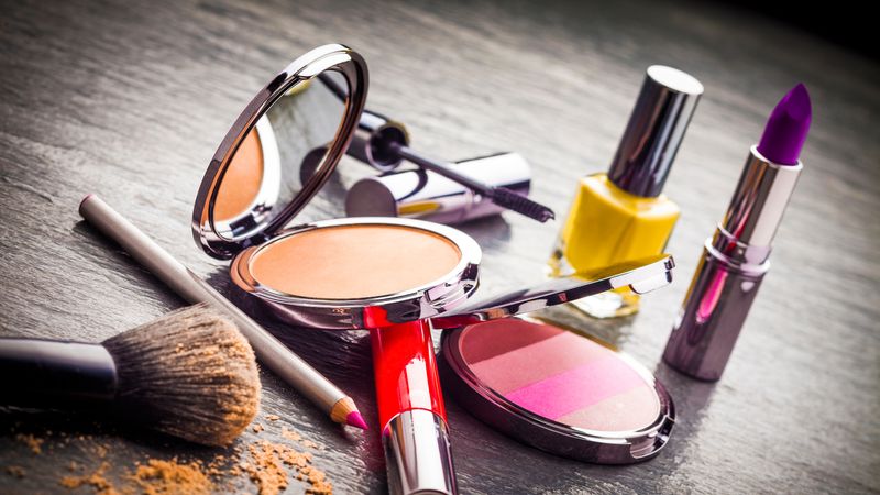 A selection of cosmetics including lipstick, nail varnish, blusher, powder brush and mascara, as if someone has turned out their make up bag on a table